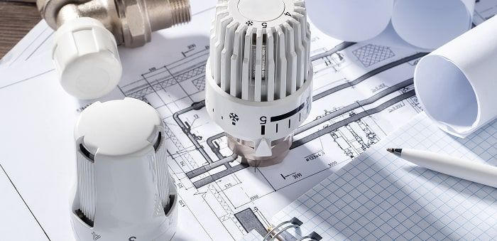 Thermostatventil und zwei weiße Heizkörperventile liegen auf einem technischen Bauplan mit Rohrleitungen und Maßen.